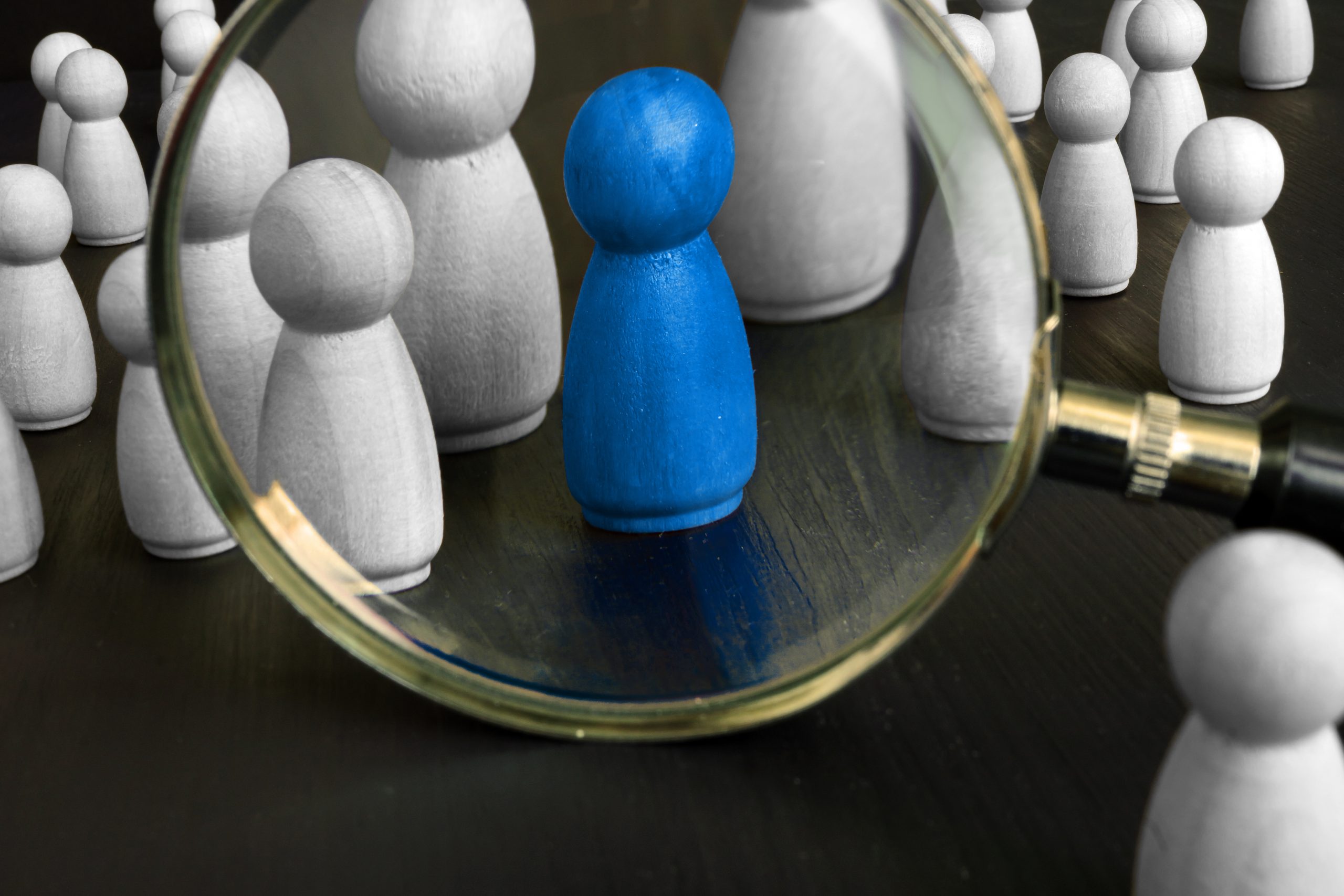 Group of wooden pawns with blue focal pawn in a magnifying glass.